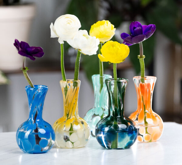 Image of 5 small glass vases with globed bases. Each vase holds a flower.